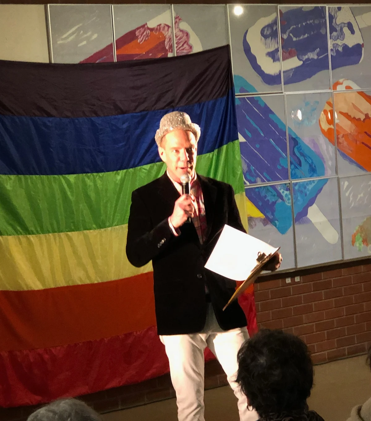 Robert Sarison holding a microphone in front of a rainbow backdrop